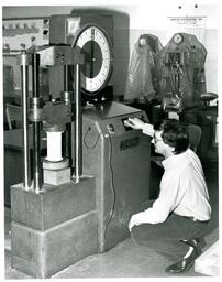 Man Squatting next to Machine and Turning Knob (Part of the NMU Historic Photographs Collection)